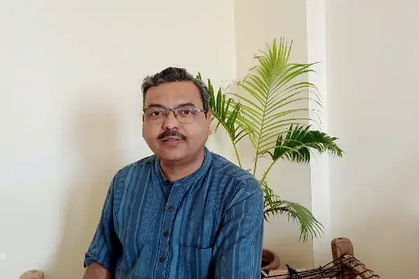 Anil Singh in a blue kurta, seated beside a leafy plant
