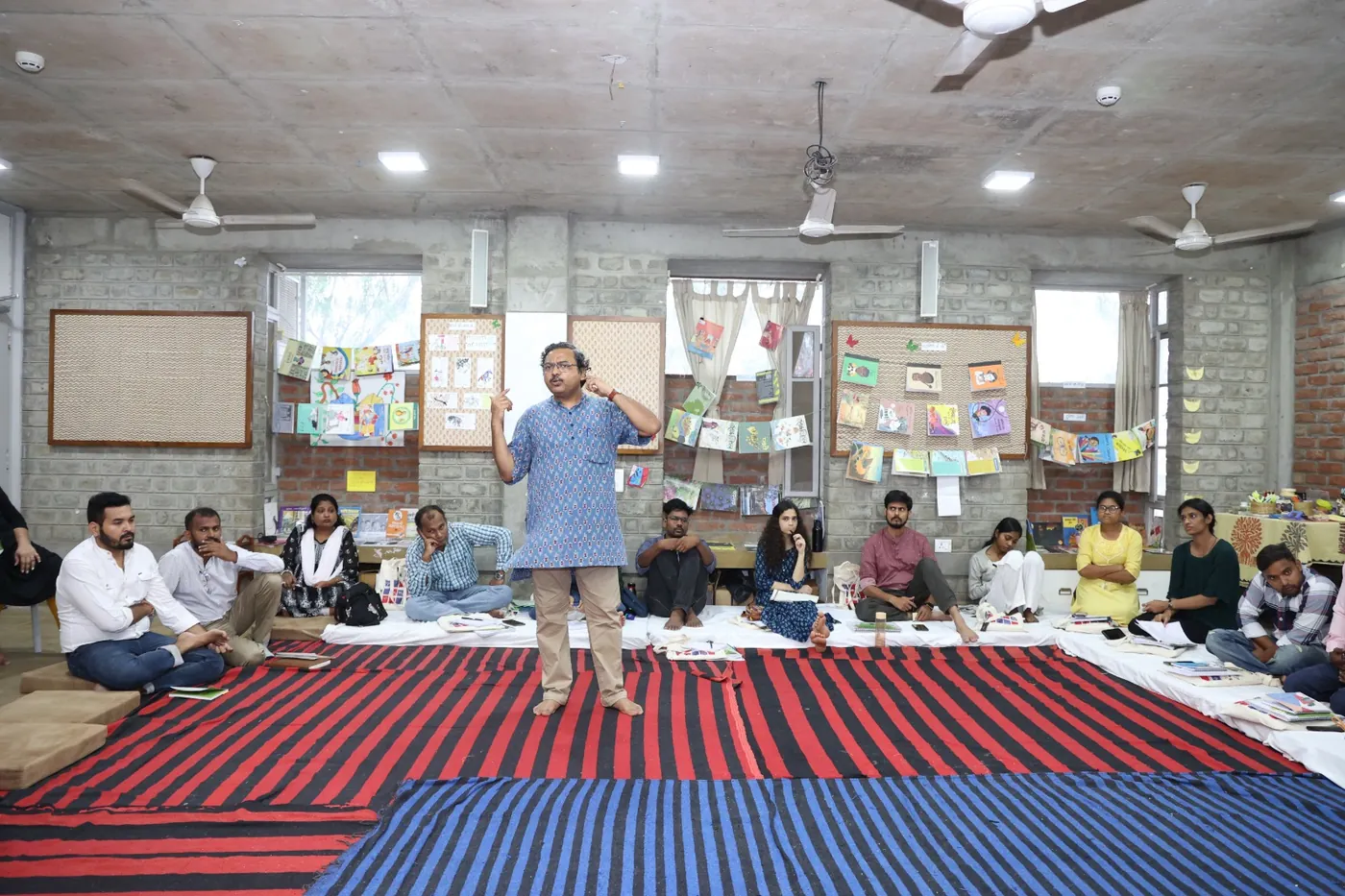 Anil speaking with a seated group in a workshop room filled with children’s books
